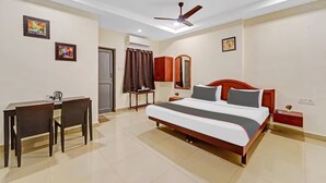 A hotel room with a bed, desk, chairs, a ceiling fan, and artwork on the walls. - GSILVER HOTEL HIMALAYA (Chennai)