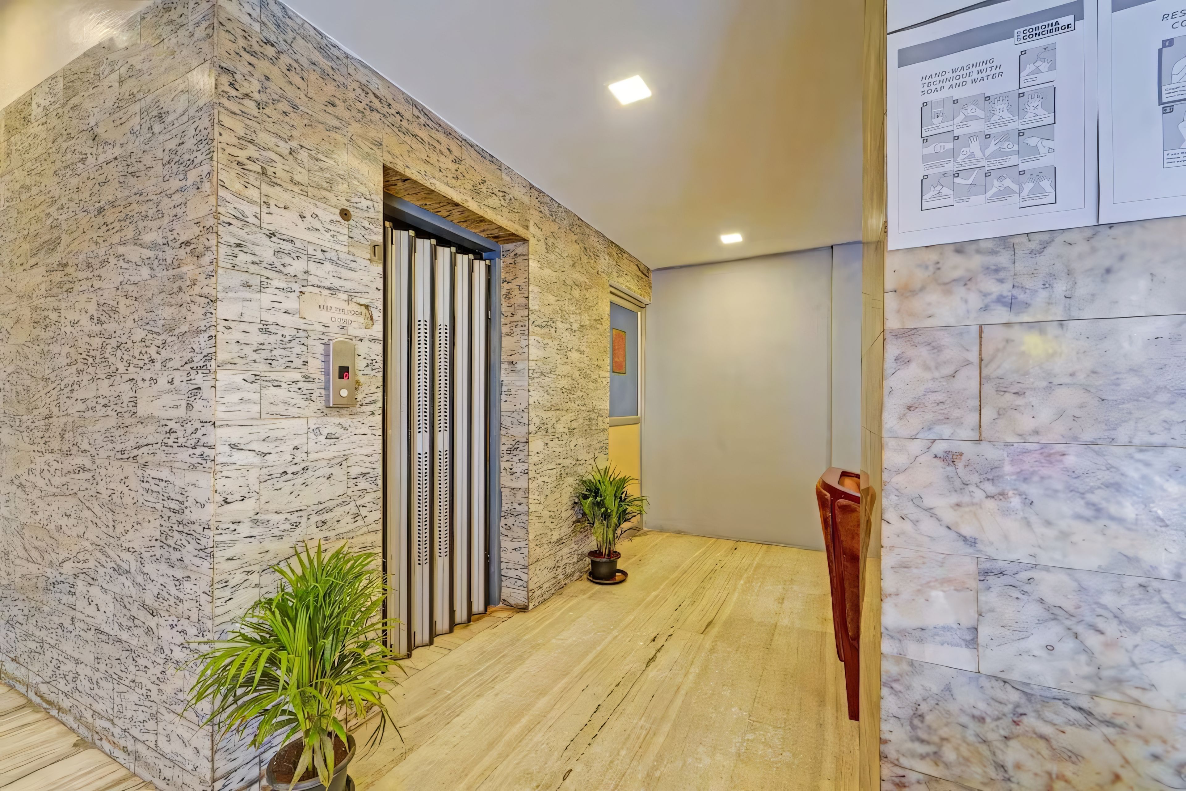 Un moderno ascensor con pantalla digital, pared de mármol con un diseño único y una planta en el vestíbulo.