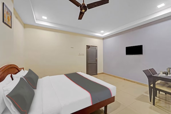 A hotel room with a bed, a desk, a chair, a ceiling fan, a television, and a door. - GSILVER HOTEL HIMALAYA (Chennai)