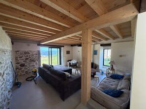 A spacious living area with a stone wall, a large sofa, a smaller sofa, and a view of the outdoors. - Casa Lareira (Valdoviño)