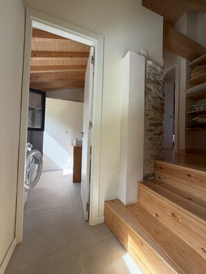 A staircase leading to a second floor with a stone wall and wooden beams. - Casa Lareira (Valdoviño)