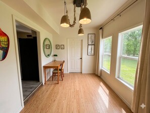 Ein Zimmer mit Holzboden, einem Esstisch mit Stühlen, einer Tür und einem Fenster mit Blick ins Grüne.
