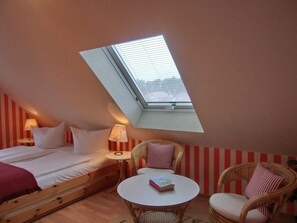 A bedroom with a skylight, a bed, a bedside table with a lamp, a small round table with a book, and two wicker chairs. - Holiday Home in Graal-muritz With Terrace (Graal Mueritz)