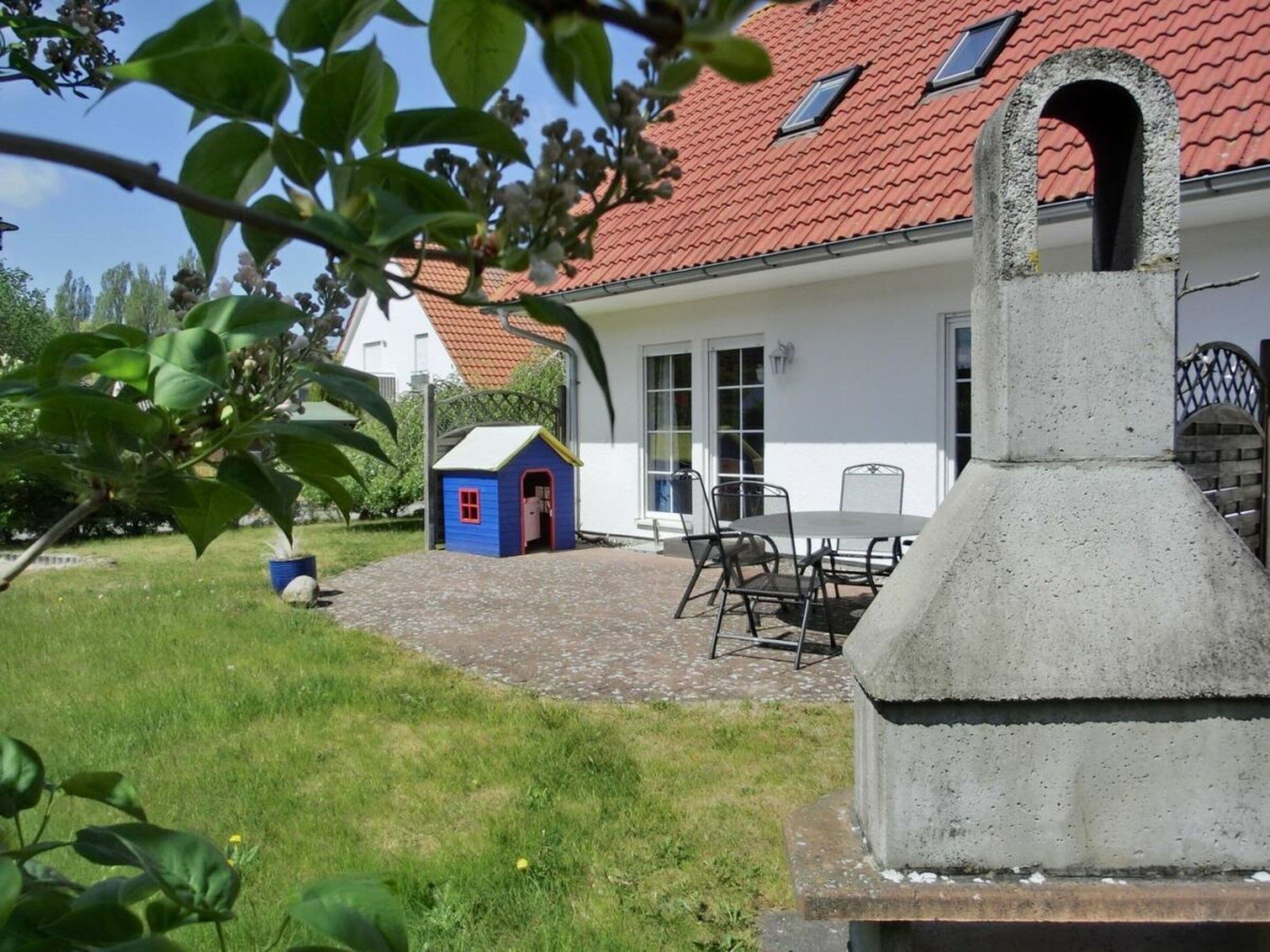 A house with a red-tiled roof, a small blue playhouse, a barbecue area, and a paved patio.