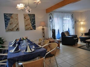 A dining area with a table set for four, a computer on a side table, and a living room with a sofa and armchairs. - Holiday Home in Graal-muritz With Terrace (Graal Mueritz)