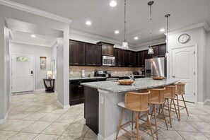Una cocina moderna con armarios de madera oscura, electrodomésticos de acero inoxidable, encimera de granito y una isla central con taburetes de bar.