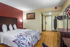 Een hotelkamer met een groot bed, een bureau, een stoel, een kledingkast, een deur en een tv aan de muur.