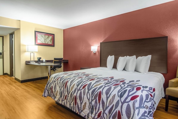 A hotel room with a large bed, a desk with a chair, a lamp, and a framed picture on the wall.