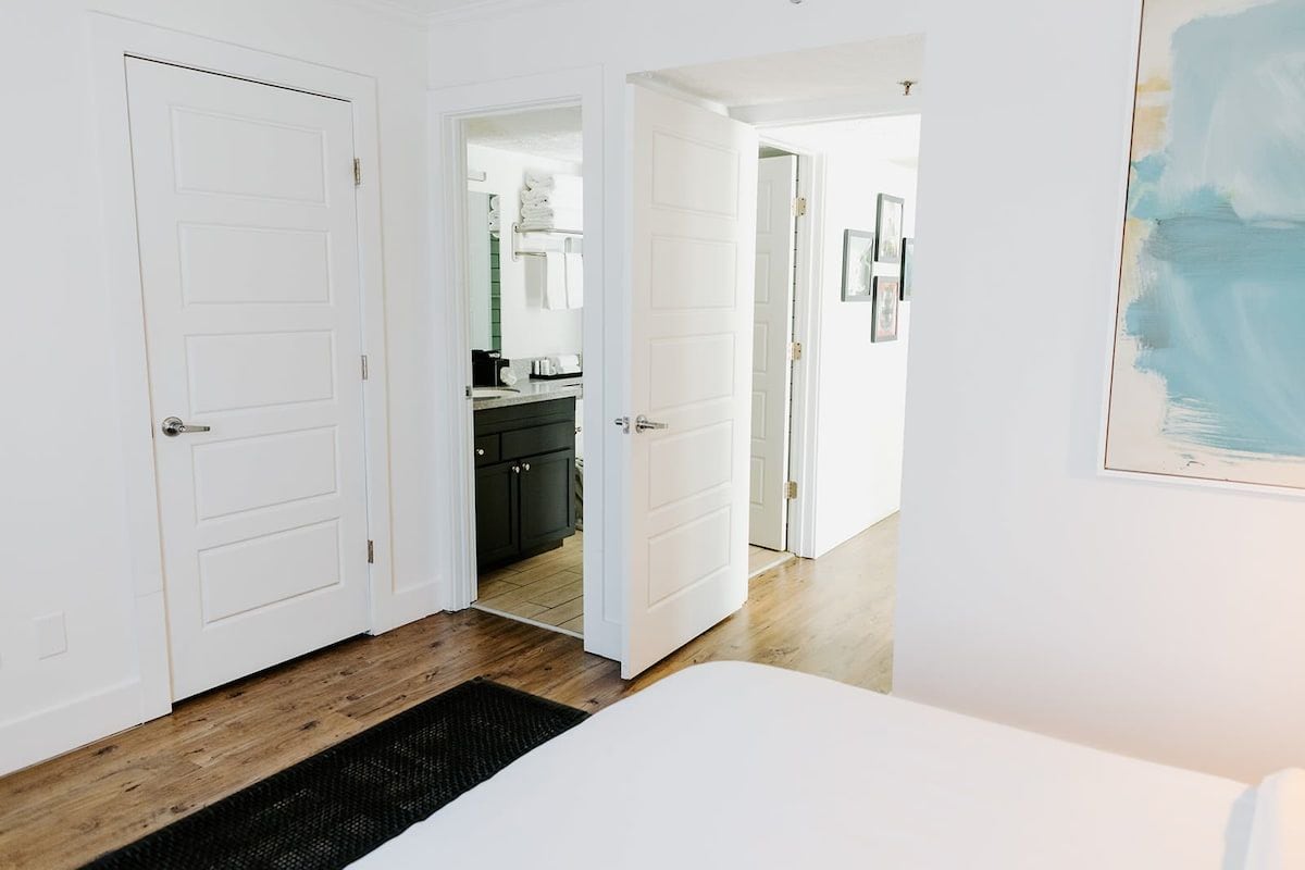 A bedroom with a bed, a black rug, and a white door leading to a bathroom.
