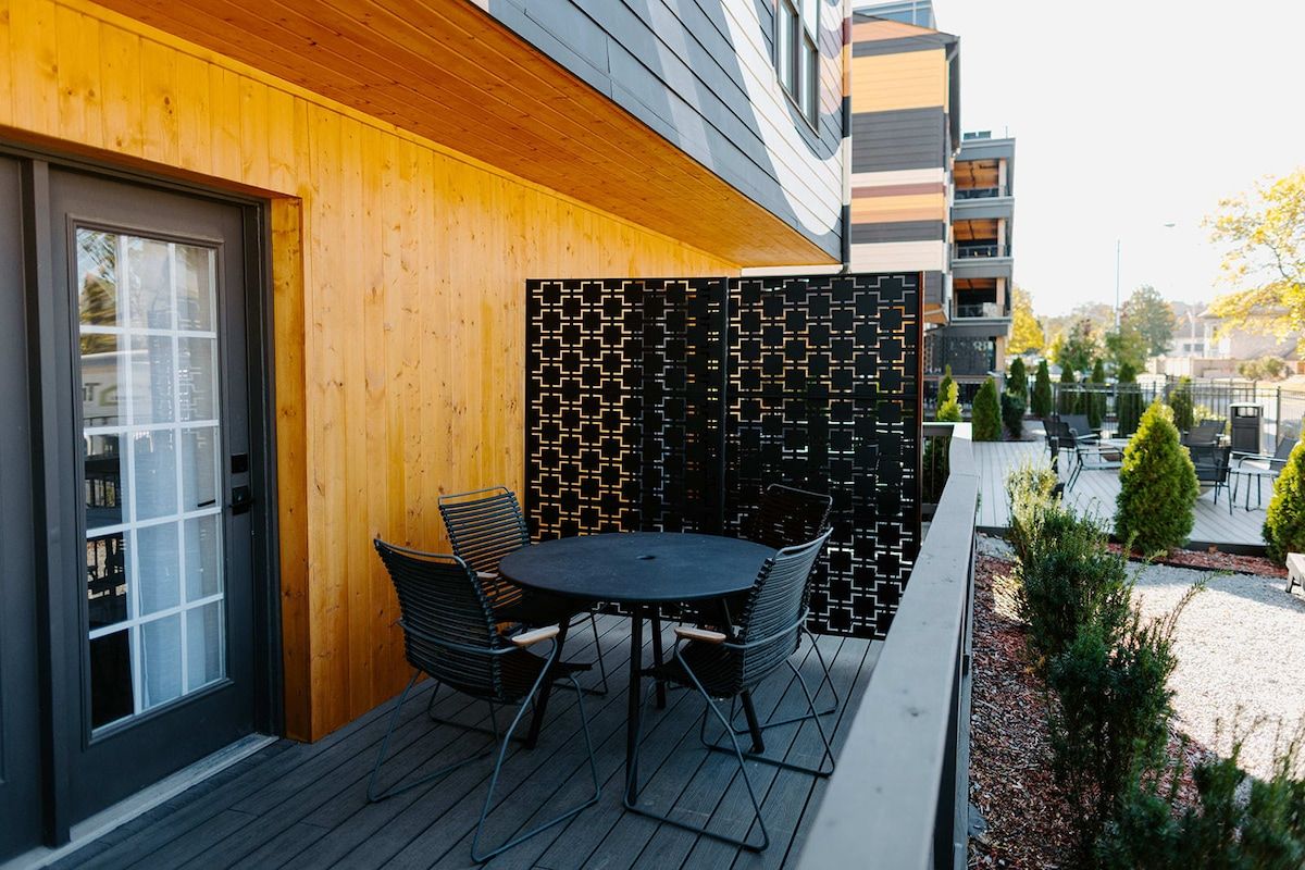 An outdoor seating area with a round table and chairs, a wooden wall, and a patterned fence.