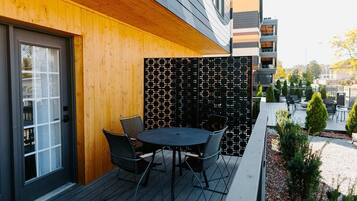An outdoor seating area with a round table and chairs, a wooden wall, and a patterned fence.