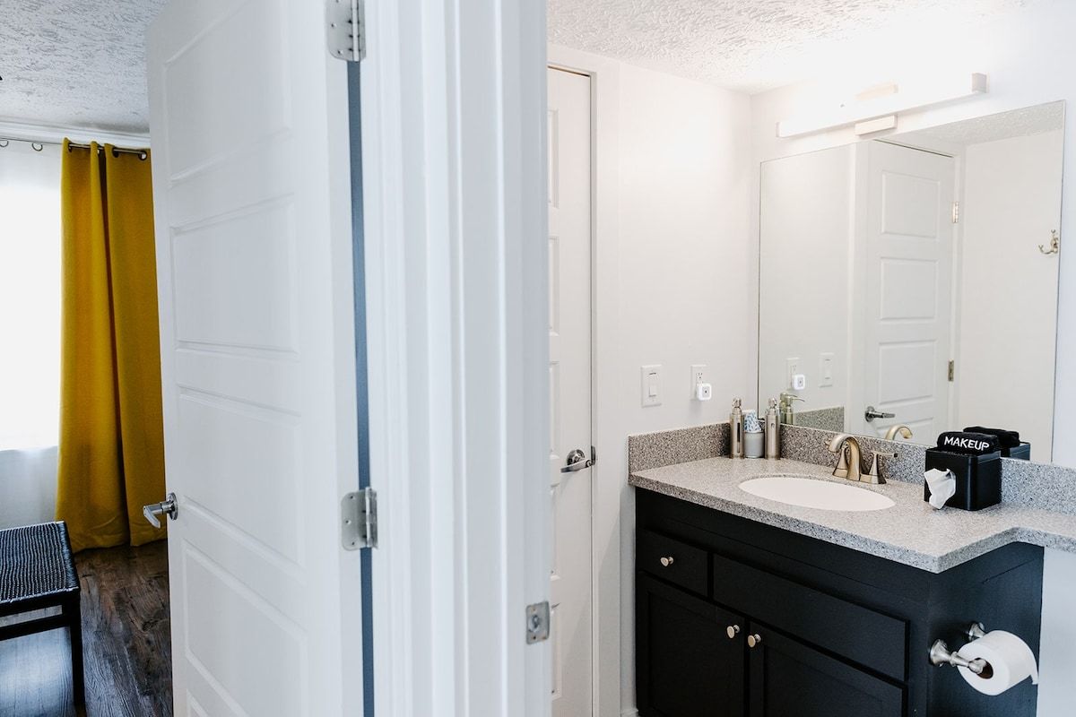 Un baño con lavamanos blanco, espejo y mueble de tocador negro.