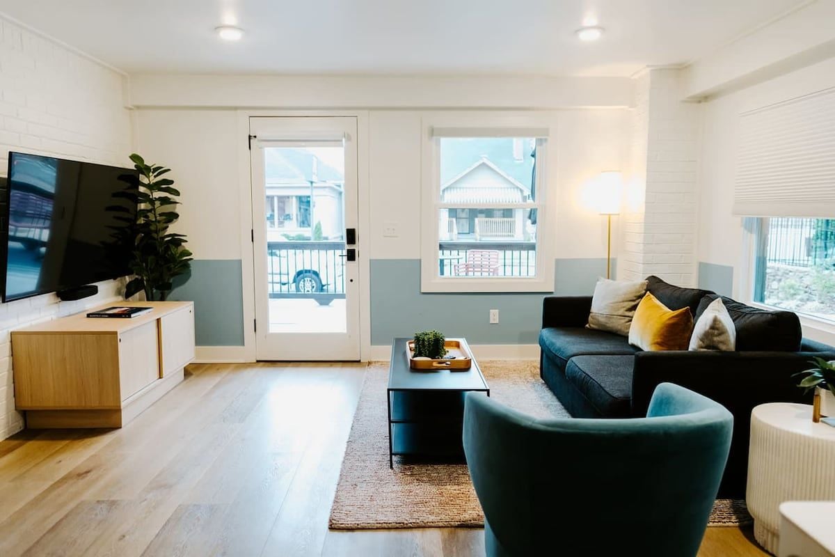 A modern living room with a flat-screen TV, a sofa, a coffee table, and a plant.