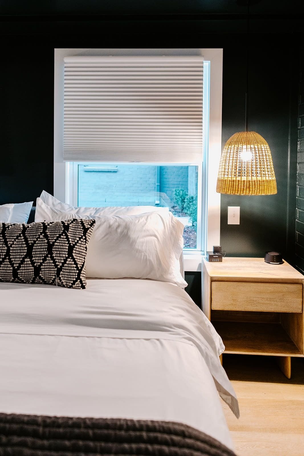 A bedroom with a bed, a bedside table, a lamp, and a window with blinds.