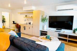 Una sala de estar moderna con un sofá, una mesa de centro, un televisor de pantalla plana y una cocina con armarios y un microondas.