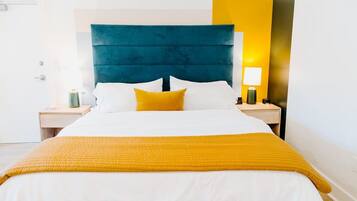 A hotel room with a large bed, a headboard, a bedside table, a lamp, and a wall-mounted light fixture.