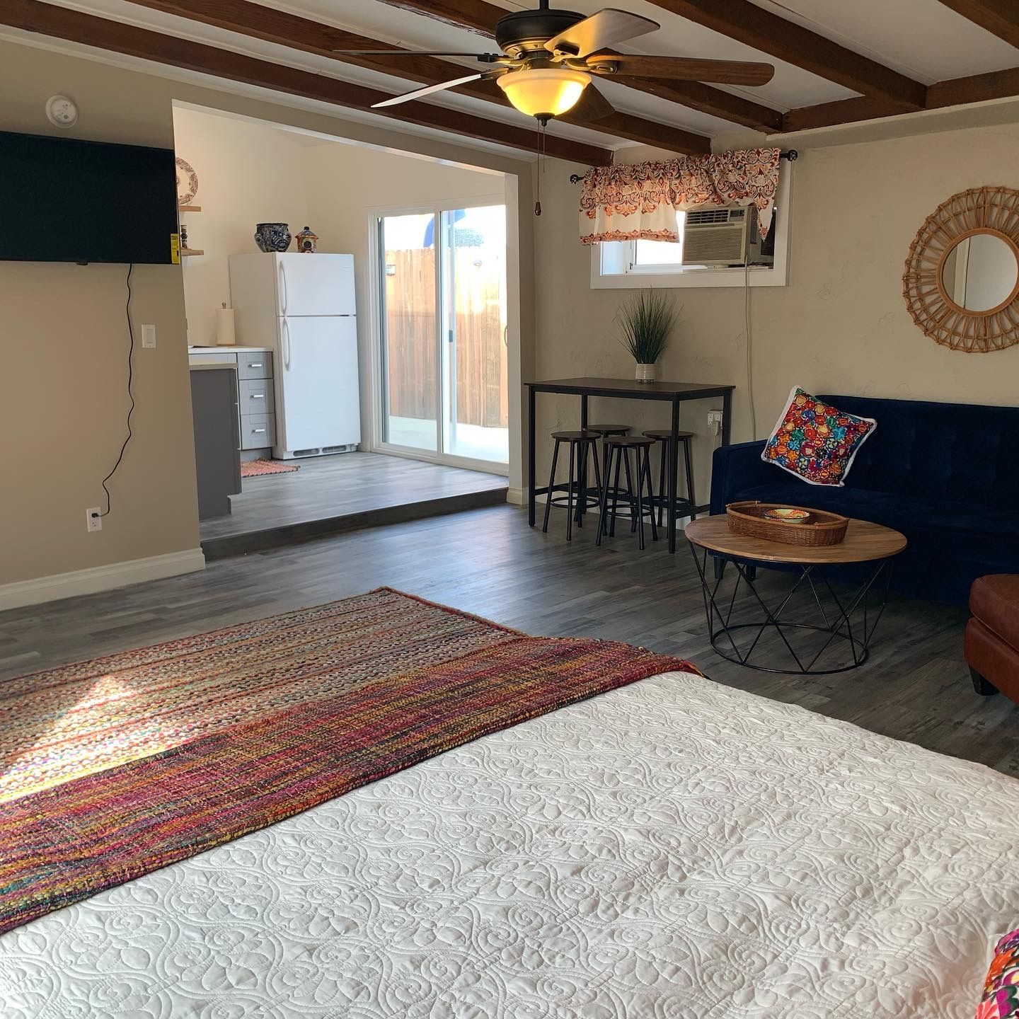 A bedroom with a bed, a dining area with a table and chairs, a ceiling fan, and a sliding glass door leading to a patio.