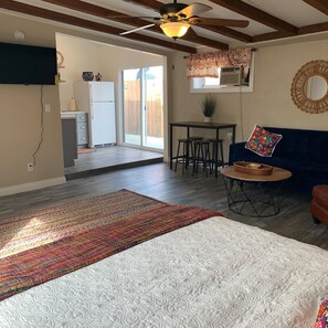 A bedroom with a bed, a dining area with a table and chairs, a ceiling fan, and a sliding glass door leading to a patio.