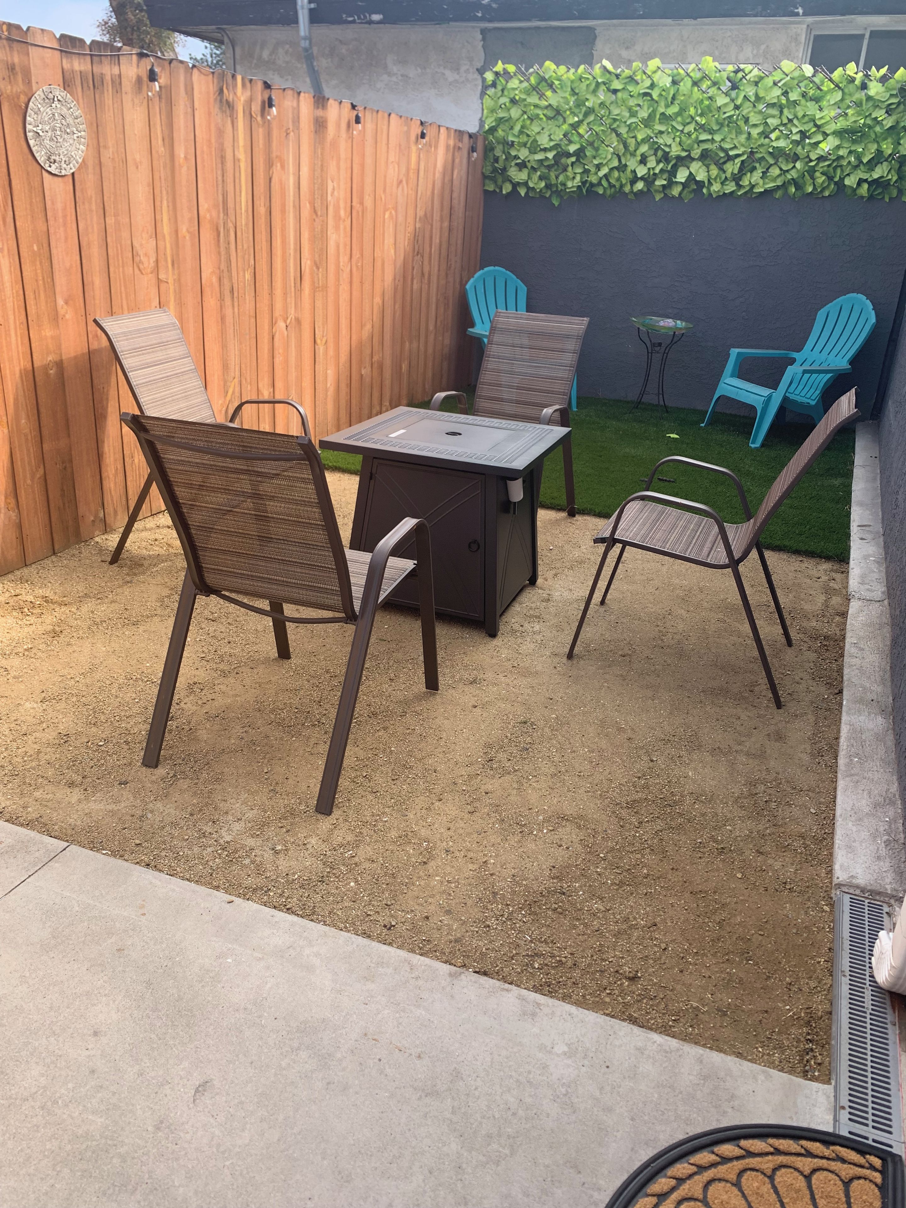 A patio with a table and chairs, a wooden fence, and a green hedge.
