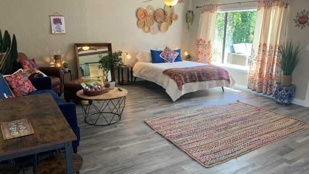 Een gezellige kamer met een bed, een eettafel, een salontafel en een groot raam met gordijnen.