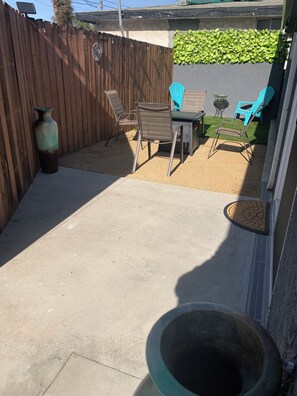 Un espace extérieur aménagé en patio, avec un sol en béton, une clôture en bois et une table entourée de chaises.