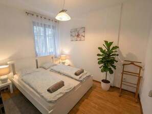 Ein Schlafzimmer mit einem Bett, Nachttischlampen, einer Topfpflanze und einem Holzkleiderständer.