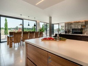 A modern kitchen with a large island, dining area with chairs, and a view of greenery outside. - Villa in Visnjan With Swimming Pool (Visnjan)