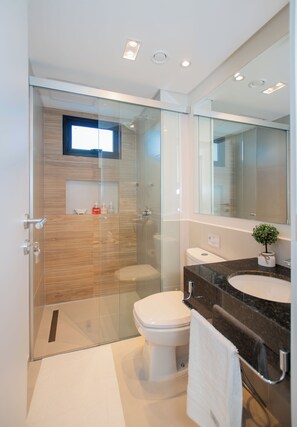 Un baño moderno con ducha envuelta en vidrio, inodoro blanco y encimera de mármol con lavamanos.