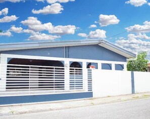 A building with a garage entrance, a white wall, and a blue roof. - Cozy 2 bedroom house in Trincity (Trincity)