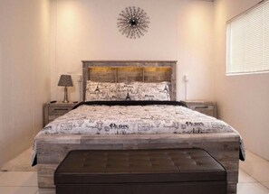 A bedroom with a bed, a nightstand, a lamp, and a decorative wall piece. - Cozy 2 bedroom house in Trincity (Trincity)