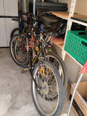 Una bicicleta en un garaje con piso de concreto, una estantería con una caja verde y una caja de cartón.