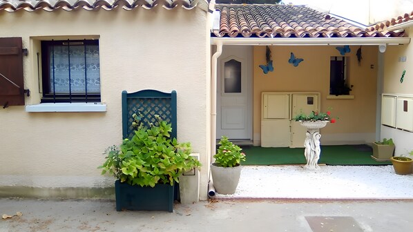 Un edificio residencial con techo de tejas, una puerta con ventanal y un pequeño jardín con macetas.