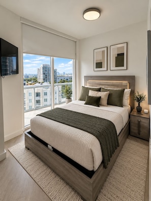 A modern bedroom with a large bed, a nightstand, a TV, and a city view. - 3BR Edgewater High Rise Bay & Skyline Views (Miami)