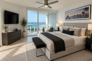 A modern bedroom with a large bed, a flat-screen TV, a balcony with a city view, and a ceiling fan. - 3BR Edgewater High Rise Bay & Skyline Views (Miami)