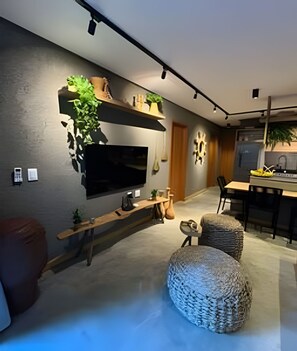 Ein modernes Wohnzimmer mit Flachbildfernseher, Holzregalen und einem Essbereich mit Tisch und Stühlen.