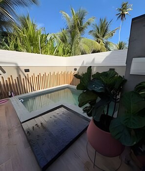 Ein Swimmingpool mit Holzzaun, umgeben von tropischen Pflanzen und Palmen.