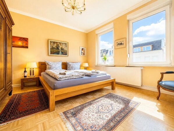 Ein Schlafzimmer mit einem Bett, zwei Nachttischen, einer Deckenleuchte, einem Fenster mit Aussicht und einem Sessel.