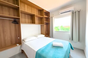 A hotel room with a bed, wooden wardrobe, and a window with curtains. - Apartamento 3 com 2 suítes 450m da praia (Santa Cruz Cabrália)