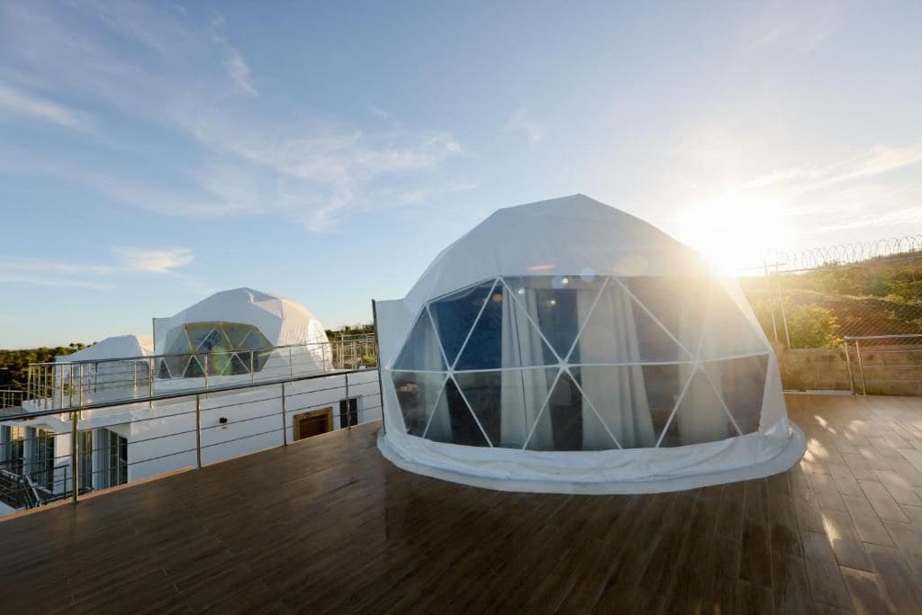 Una estructura arquitectónica moderna con diseño abovedado, que presenta una sección transparente y un exterior blanco.
