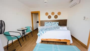 Een hotelkamer met een bed, een tafeltje, twee stoelen, een ventilator en een airconditioner aan de muur.
