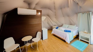 Ein gemütliches Zimmer mit einem Bett, einem kleinen Tisch, zwei Stühlen, einem Nachttisch und einem Fenster mit Vorhängen.