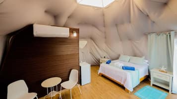 Una habitación acogedora con cama, una mesita, dos sillas, una mesita de noche y un ventanal con cortinas.