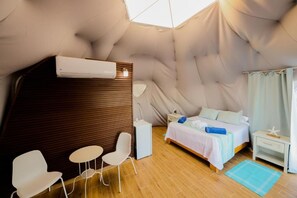 Ein gemütliches Zimmer mit einem Bett, einem kleinen Tisch, zwei Stühlen, einem Nachttisch und einem Fenster mit Vorhängen.