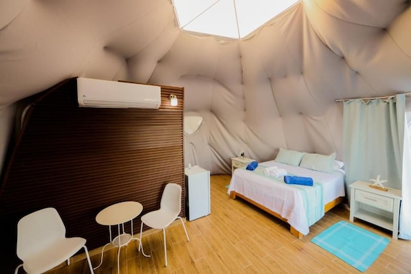 A cozy room with a bed, a small table, two chairs, a bedside table, and a window with curtains.