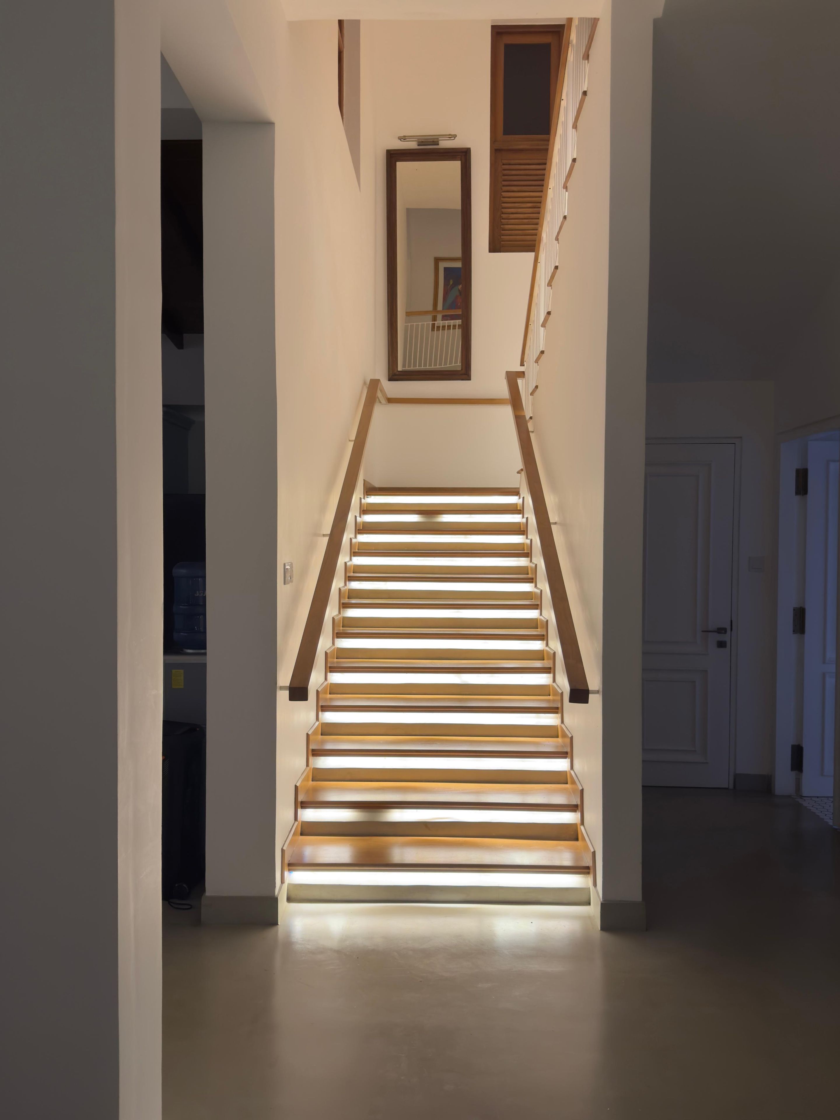 A staircase with wooden steps and handrails, leading to a landing with a mirror and a door.