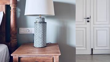 Een houten nachtkastje met een lamp en een lade, een witte deur, en een lichtschakelaar op de muur.