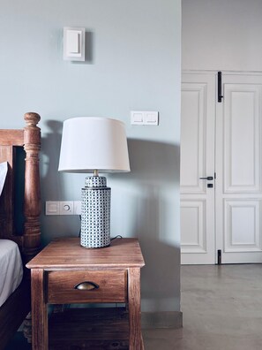 Ein Nachttisch aus Holz mit Lampe und Schublade, eine weiße Tür und ein Lichtschalter an der Wand.