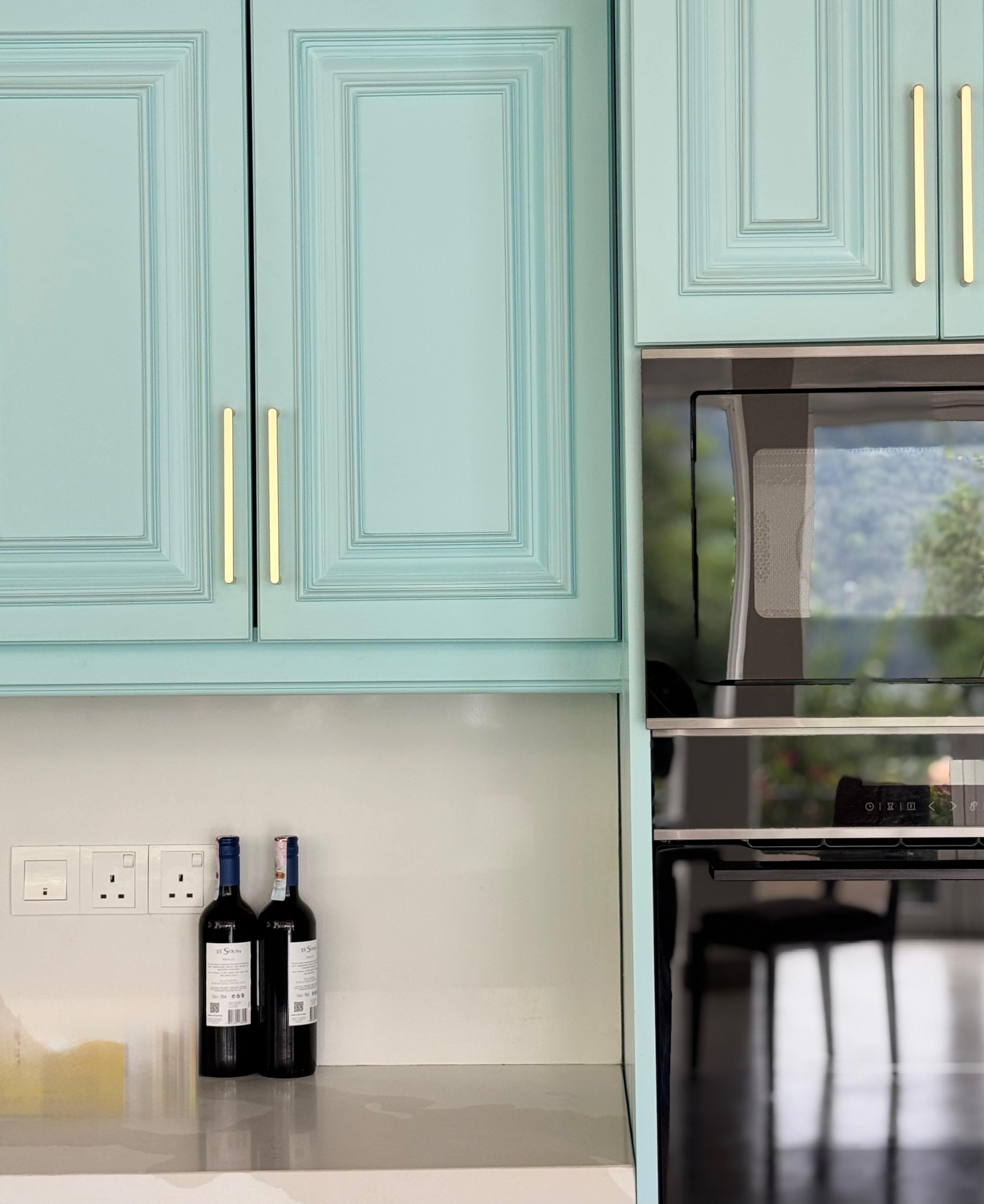 A kitchen with teal cabinets, gold handles, and a stainless steel oven.