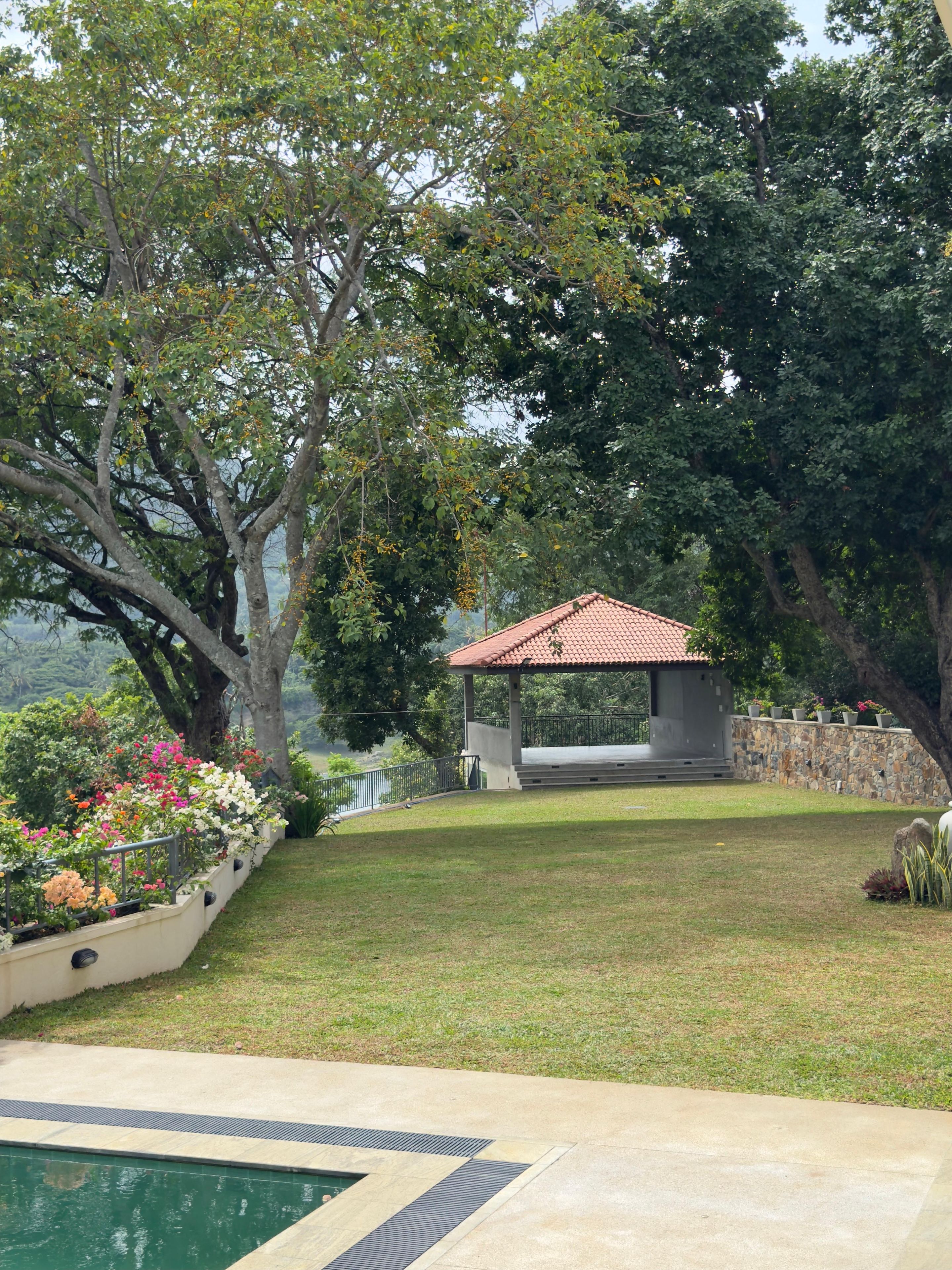 A garden with a gazebo, a swimming pool, and a stone wall.