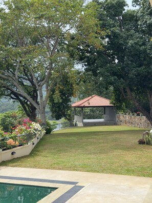 A garden with a gazebo, a swimming pool, and a stone wall. - Villa Eranya Kandy (Digana)